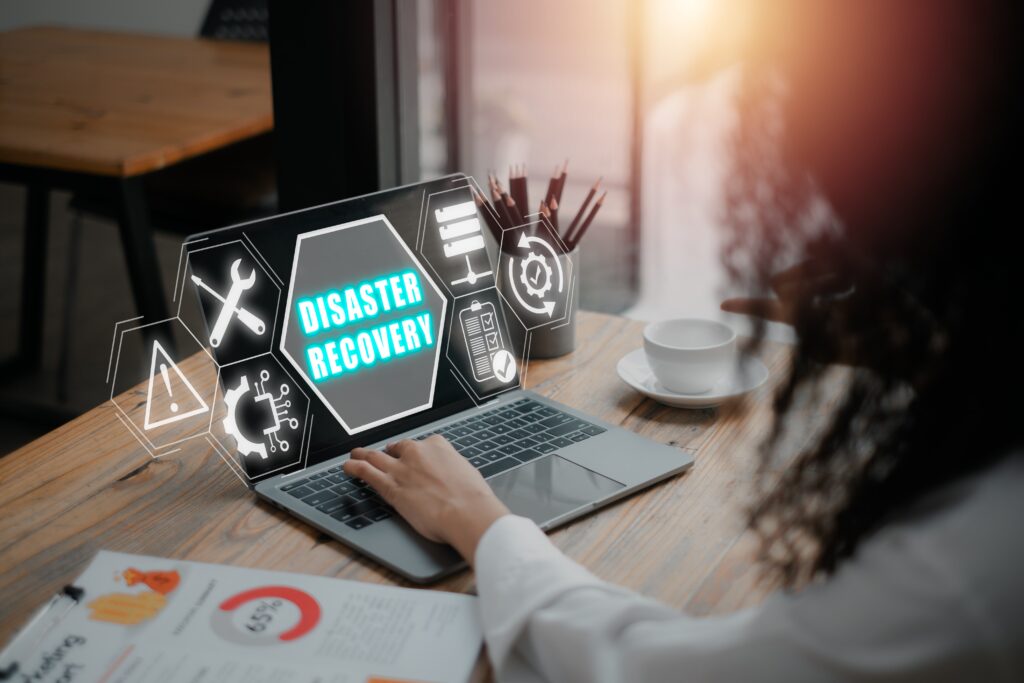 An individual working on a laptop displaying a hologram of “Disaster Recovery” and tools that contribute to an effective disaster recovery.