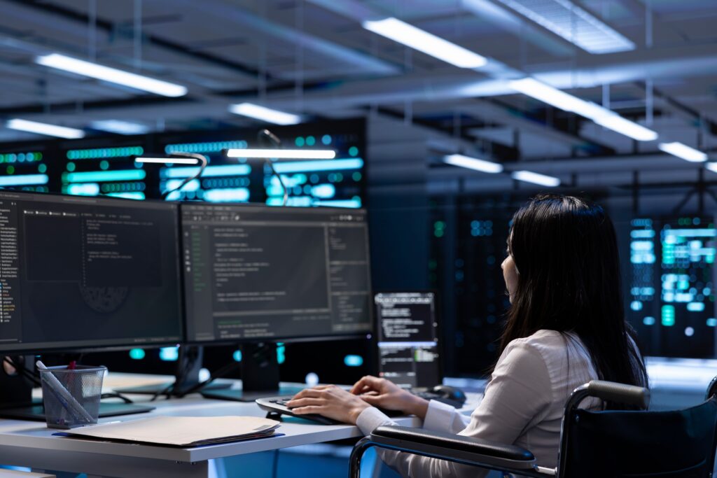 Modern cybersecurity workspace with a female IT professional in a wheelchair working at a multi-monitor setup in a high-tech server room.