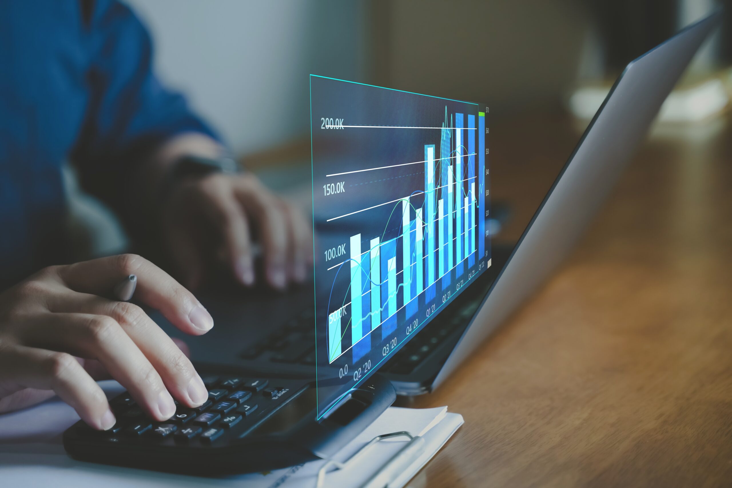 Person working on a laptop displaying a holographic bar chart with rising statistics