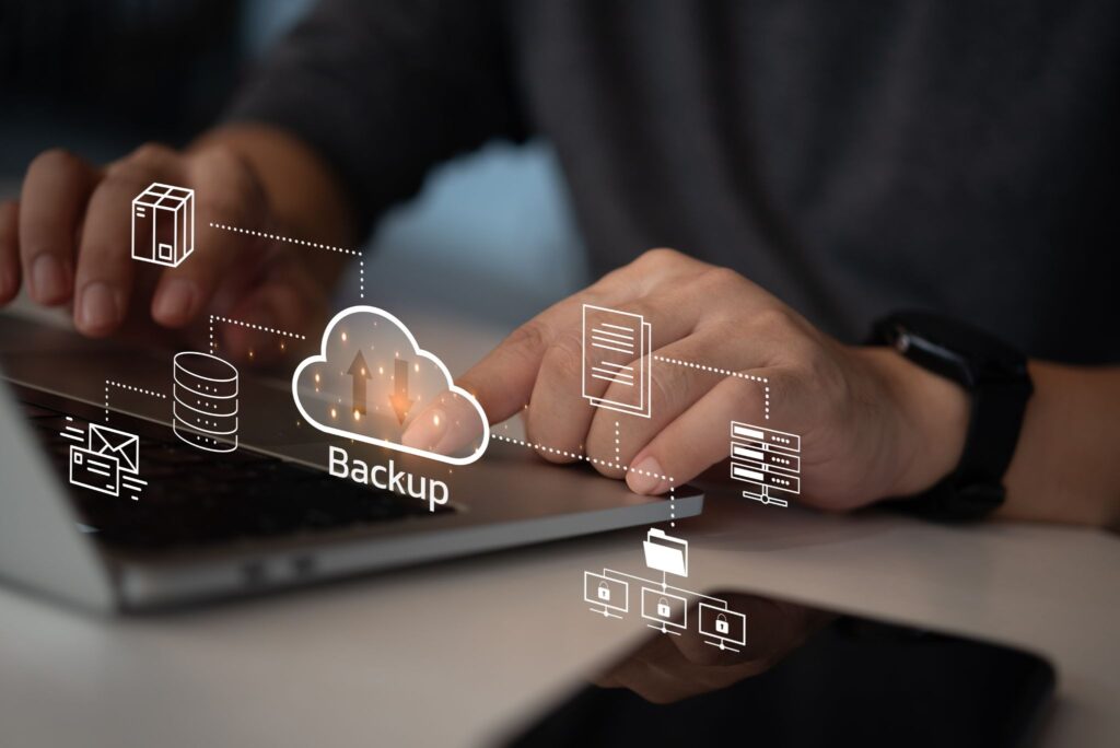 Hands typing on a laptop with digital backup icons, including a cloud, folders, and a database