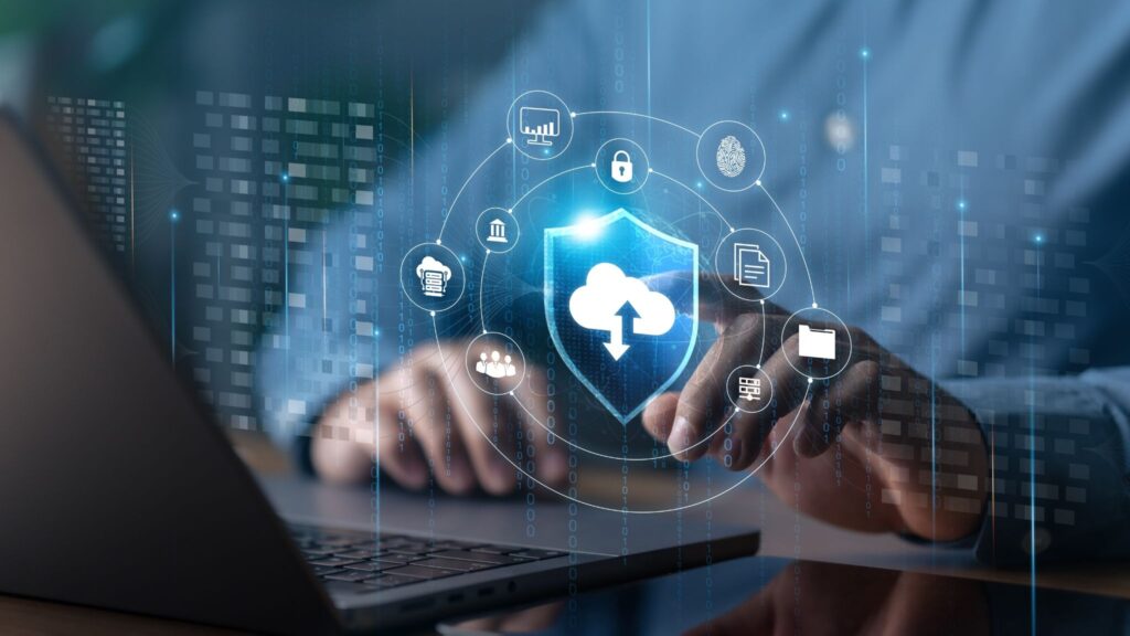 A person uses a laptop with a virtual interface showing a shield and cloud icon, surrounded by digital security and data-related icons, representing cloud computing and cybersecurity concepts.